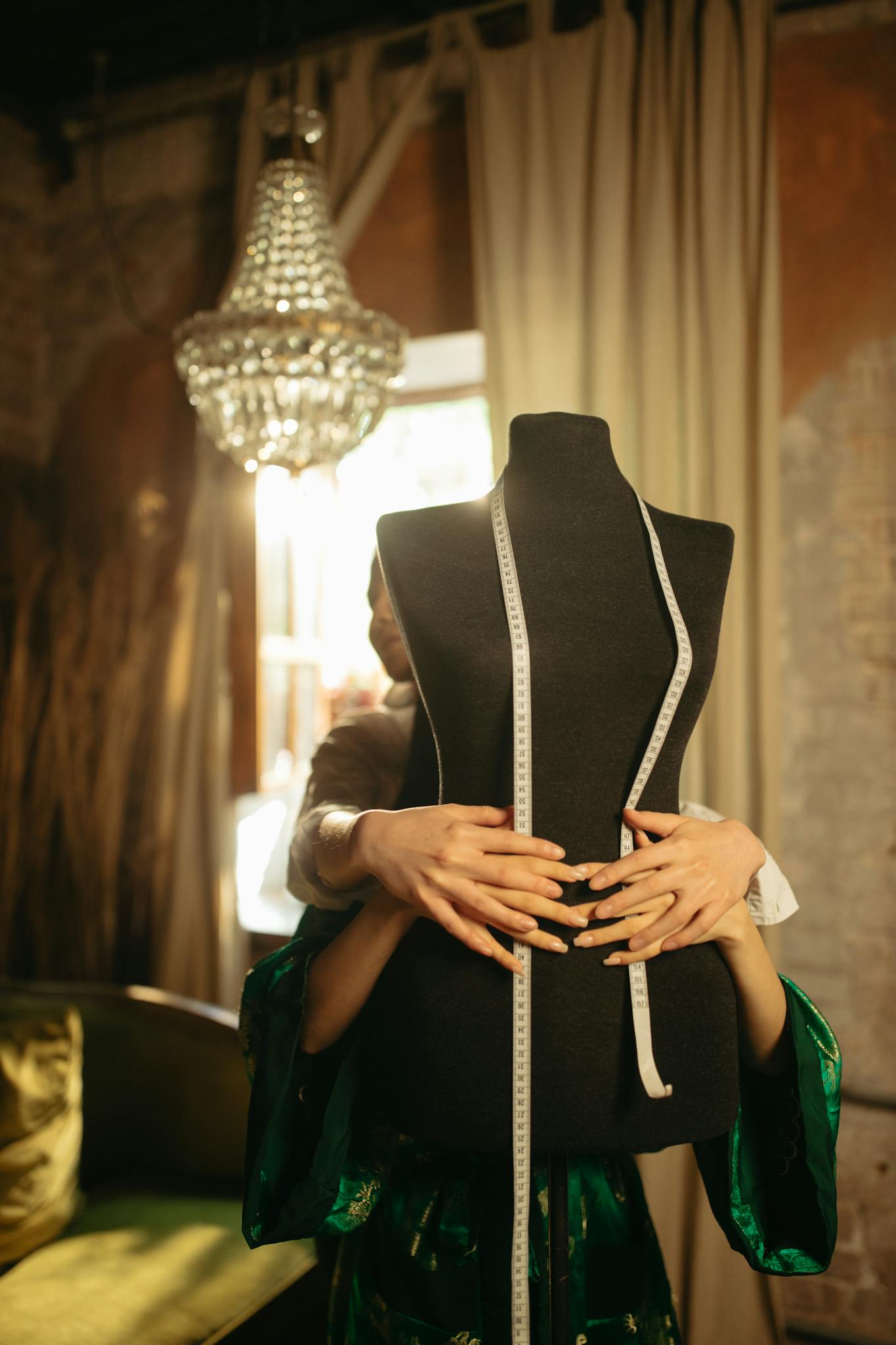 A fashion designer measures a mannequin in a stylish workshop with sunlight streaming through.